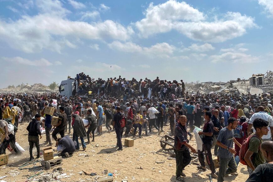 Displaced Palestinians carry food parcels as they raid trucks carrying humanitarian aid in Khan Yunis, in the southern Gaza Strip