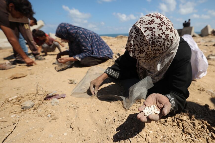 Palestinian women search the sand for legumes or rice in the central Gaza Strip during an aid airdrop mission