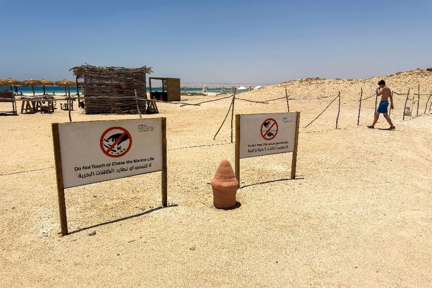 A tourist walks past signs warning people not to disturb the local marine life and wildlife at the beach at the Ras Hankorab 