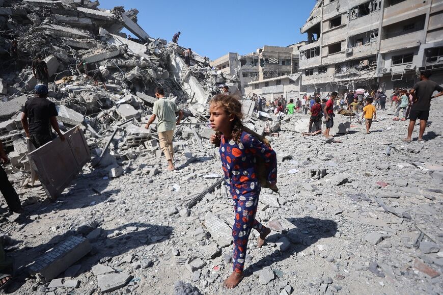 Displaced Palestinians salvage items from the rubble of the Al-Ghafari tower after it was destroyed in Israeli strikes in Gaza City