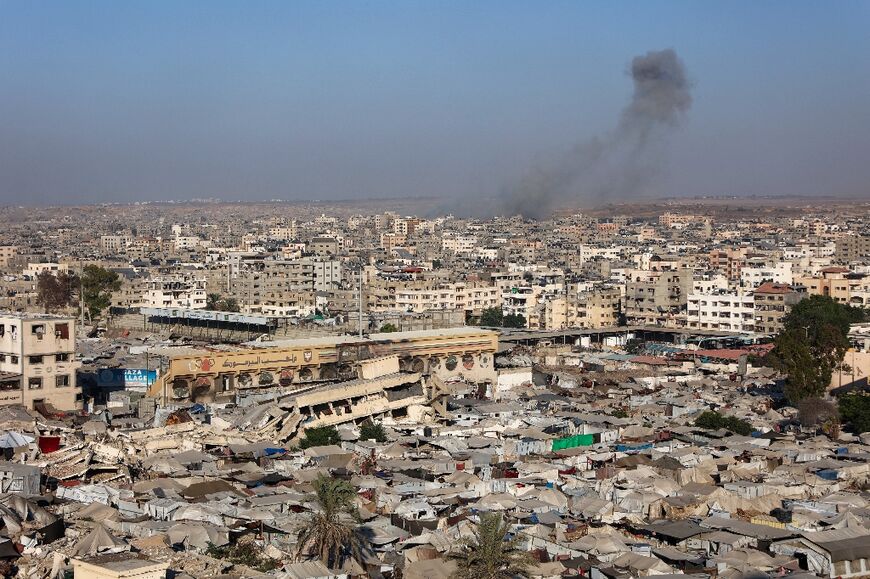 View of a makeshift displacement camp at a sports stadium in Gaza City, as smoke billows during Israeli strikes