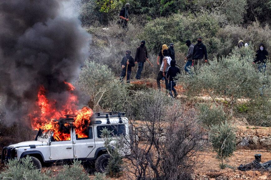 Masked men gather near a vehicle set ablaze during the attack