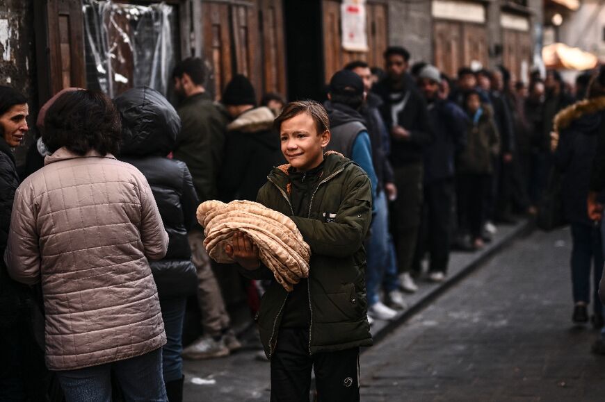 A boy carrying freshly-baked bread as people line up outside a bakery in Damascus. More than a million Syrian refugees have returned, putting pressure on the country's infrastructure