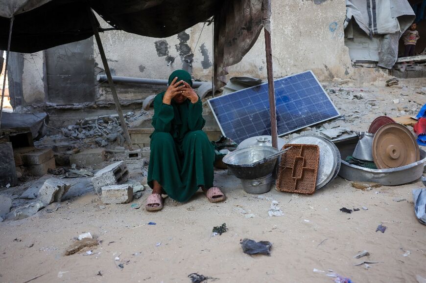 A woman reacts as she sits next to her utensils salvaged from the rubble of a house destroyed in an Israeli strike on Gaza
