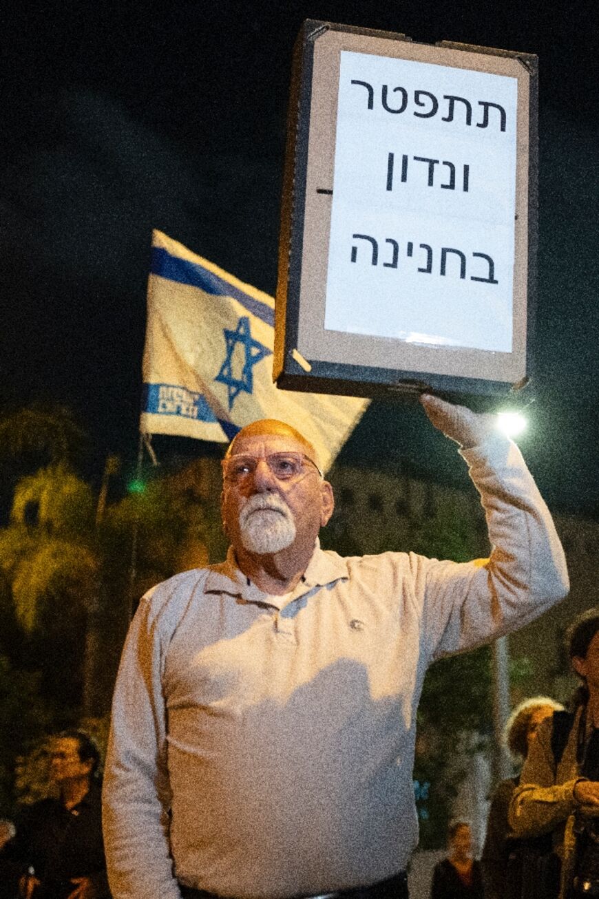A demonstrator holds a sign reading in Hebrew: 'Resign and we will discuss a pardon'