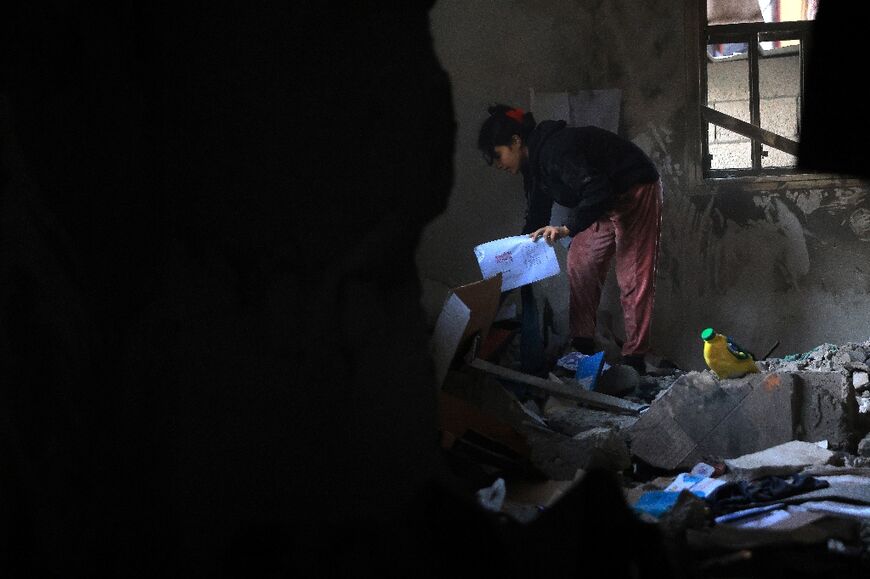A Palestinian girl picks up her school work from the debris of a destroyed house