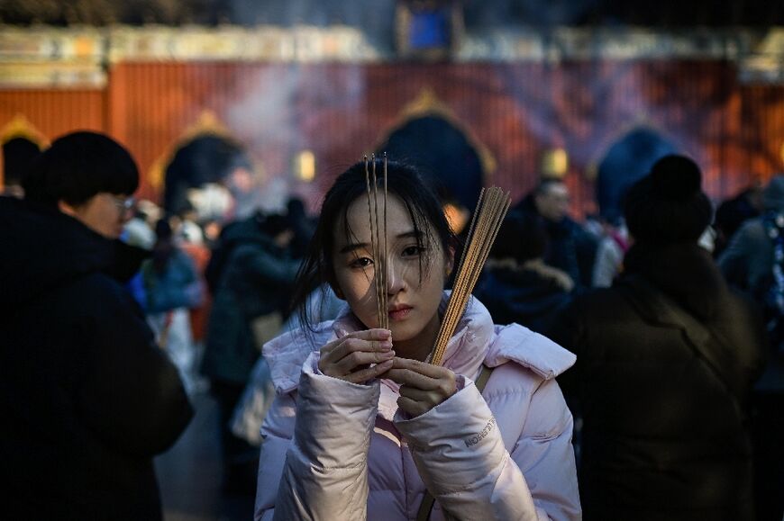 A woman burns incense sticks and offers prayers at Yonghe Temple, also known as Lama Temple, on the first day of the new year in Beijing on January 1, 2026