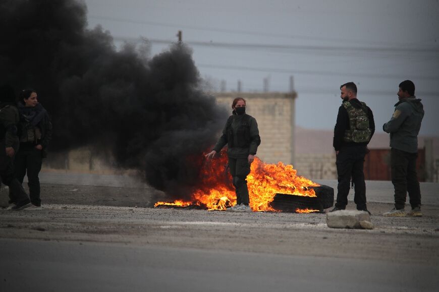 Kurdish fighters stand near burning tires at the entrance to the city of Tabqa in the northern Syrian Raqa province, on January 17, 2026