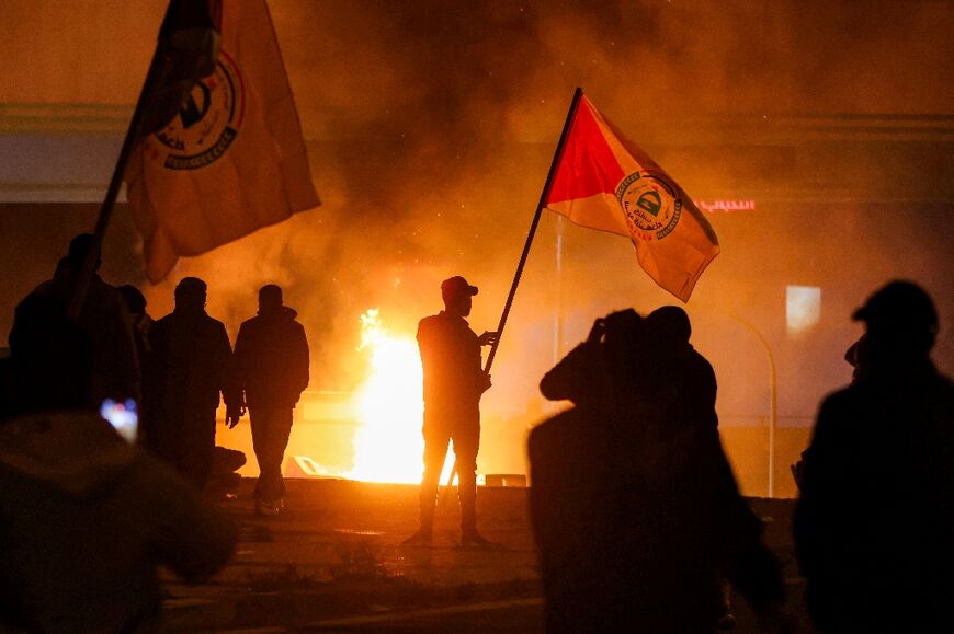 Protesters stand near a fire during clashes with Iraqi security forces as they try to approach a bridge leading to the Green Zone where the US embassy is located in Baghdad