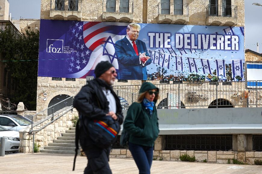 People walk past a banner in Jerusalem depicting US President Donald Trump with the slogan 'The Deliverer' in Jerusalem 