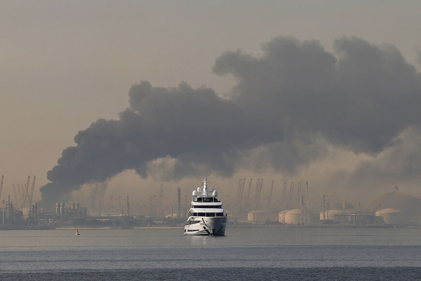 TOPSHOT - A yacht sails past a plume of smoke rising from the port of Jebel Ali following a reported Iranian strike in Dubai on March 1, 2026. Fresh blasts were heard across the Gulf cities of Dubai, Doha and Manama on Sunday morning after a day of Iran strikes in the region in retaliation for US and Israeli attacks. (Photo by Fadel SENNA / AFP via Getty Images)