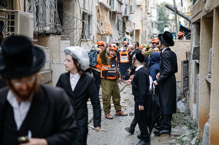 A rescuer gestures as Orthodox Jews stand at the scene of an Iranian strike over Bnei Brak in central Israel
