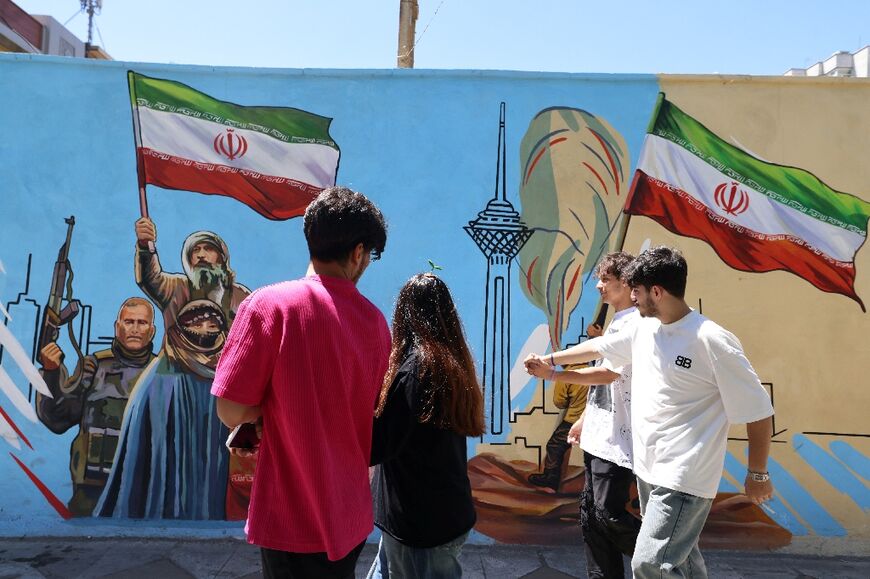 Iranians walk past an anti-US and anti-Israel mural painted on a wall in the capital Tehran