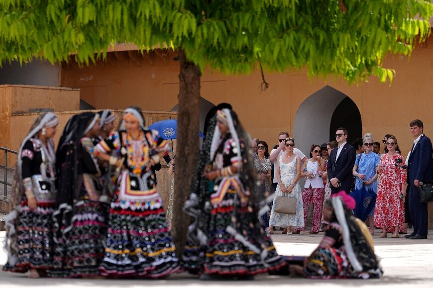 Artists wearing traditional attire and members of US Secretary of State Marco Rubio's team wait in the shade as he tours the Amber Fort in Jaipur
