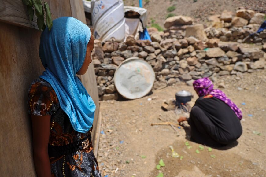 Saeedah Mohammed's grandchild watches her boiling tree leaves for food outside their makeshift tent