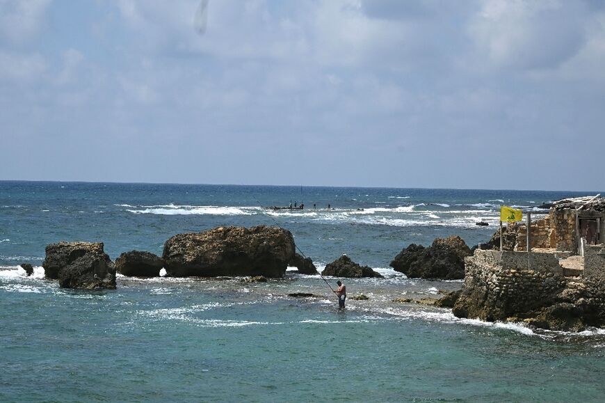 A man fishes in Tyre as a yellow Hezbollah flag flutters on the nearby shore