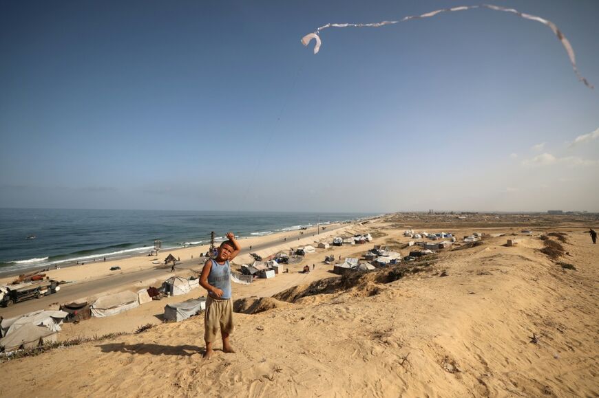 A displaced Palestinian boy flies a kite next to tents in the Nuseirat refugee camp in the central Gaza Strip in October 2025