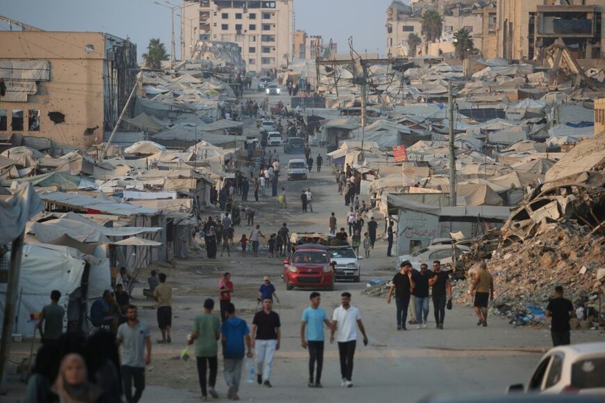 Displaced Palestinians walk past tents and destroyed buildings near the beach front in Gaza City