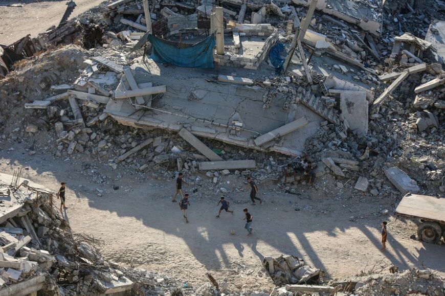 Children play football amid the ruins of destroyed buildings in Gaza City on July 27, 2026