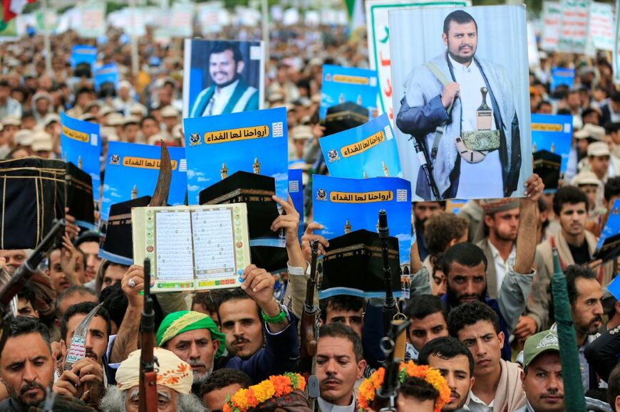 Supporters of the Houthis brandish weapons and hold up placards showing the Kaaba and reading "For it, we willingly offer our souls" during a protest against Saudi Arabia's recent accusation that the Houthis fired at the holy city of Mecca
