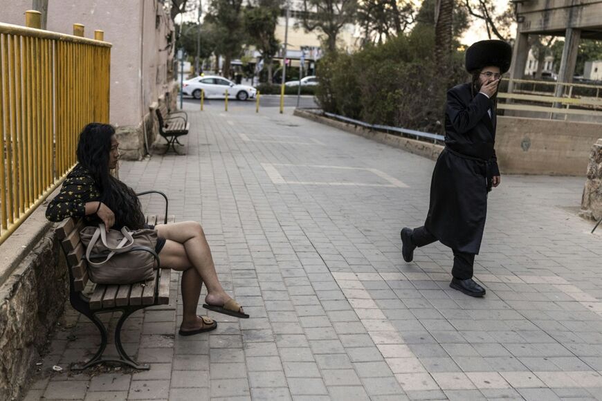 An ultra-Orthodox Jewish man walks past a woman sitting on a public bench in Arad on October 1, 2026. Ultra-Orthodox Jews are projected to account for roughly one-quarter of the Israeli population by mid-century.