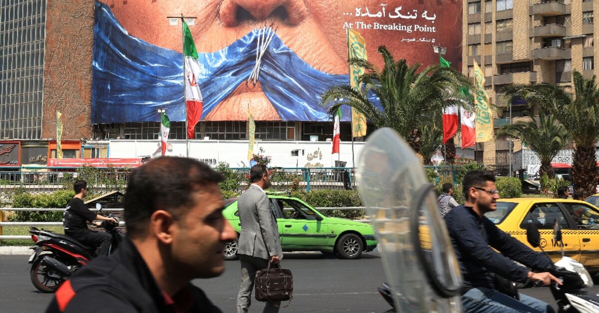 Commuters make their way past an anti-US billboard referring to President Donald Trump and the Strait of Hormuz, installed on a building at the Valiasr Square in Tehran
